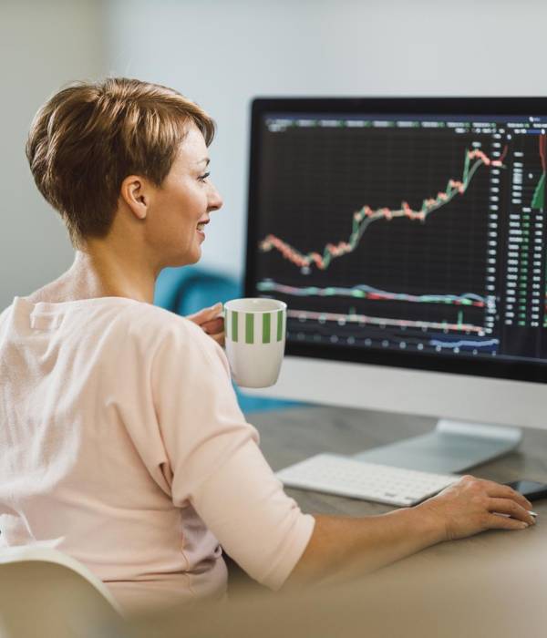 Middle age woman trading with cryptocurrency while working on computer at home office.She is monitors her investments in the stock markets.